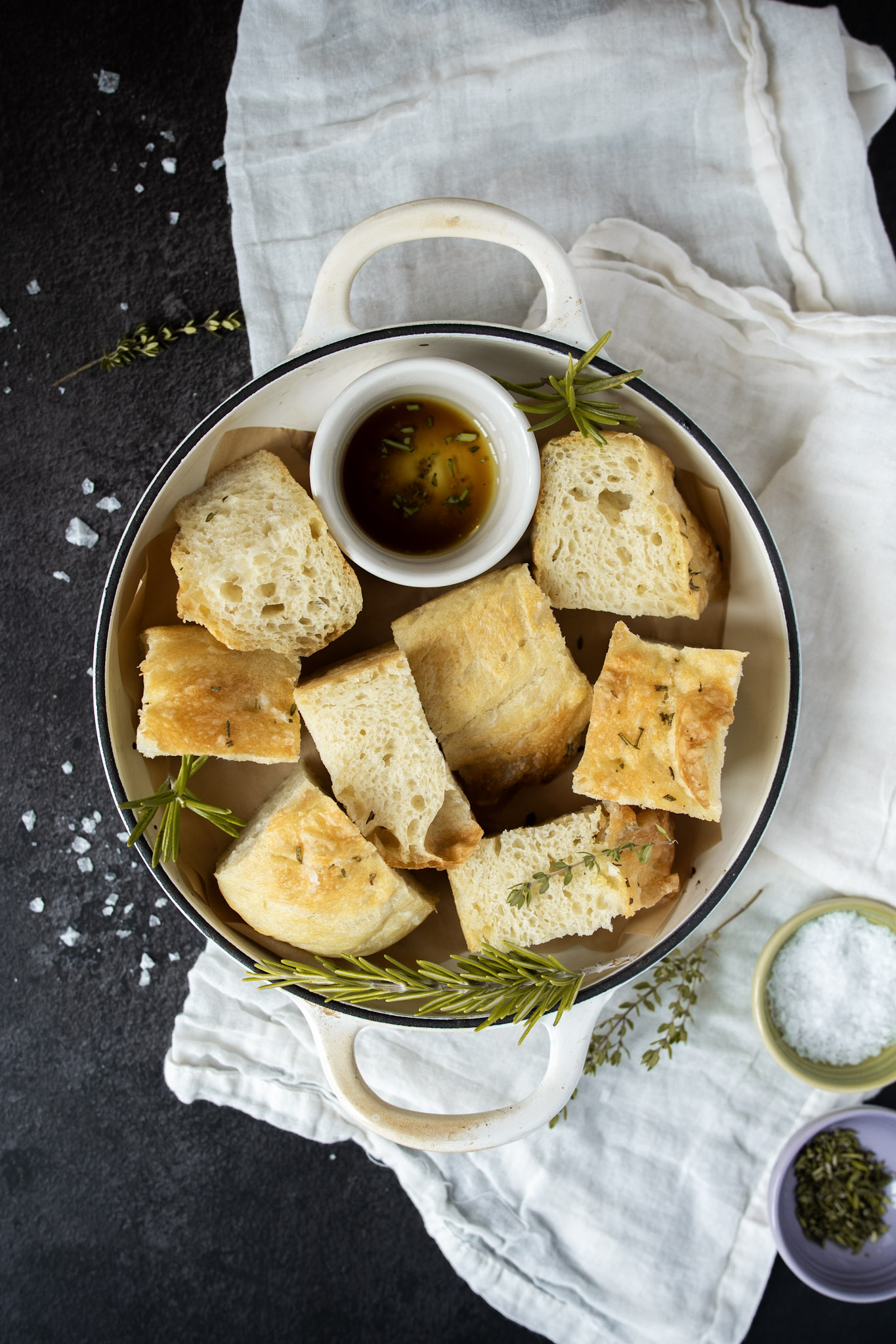 Slices of focaccia in a white dish with herbs and salt sprinkled around
